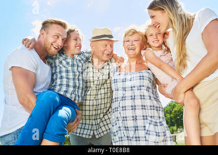 Trois générations de la famille avec les grands-parents et enfants rit joyeusement à l'appareil photo Banque D'Images