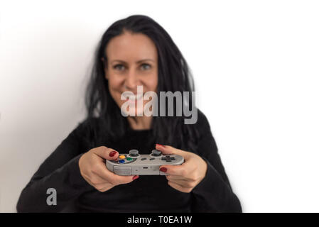 Jeune femme avec du vernis à ongles rouge playing video game sur un contrôleur de jeu sans fil rétro avec un heureux et concentré d'expressions du visage Banque D'Images