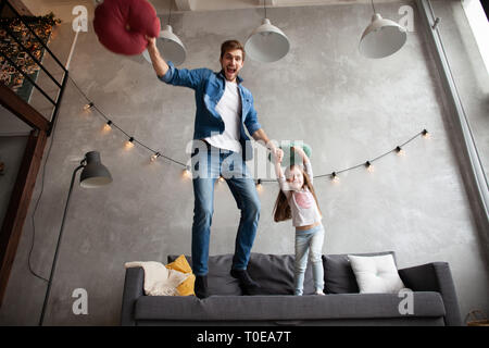 Drôle de père et fille cute kid jumping rire s'amuser dans la salle de séjour, la famille active bénéficiant d'aller jouer avec les parents à la maison. Banque D'Images