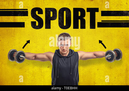 Close-up of young fit man dans sleeveless hoody latéral faisant soulever avec les haltères contre mur jaune avec le titre LE SPORT. Banque D'Images