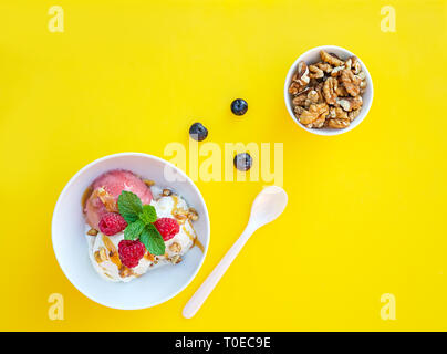 Vanille et Fraise avec crème glacée caramel et menthe sur bol blanc avec les écrous et les bleuets sur fond jaune. Trois boules, beau dessert. Coup de frais généraux. Banque D'Images