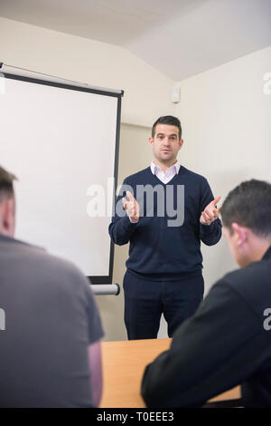 Un homme blanc dans un cavalier bleu est titulaire d'une présentation de formation pour d'autres collègues de travail dans un bureau, salle de réunion Banque D'Images