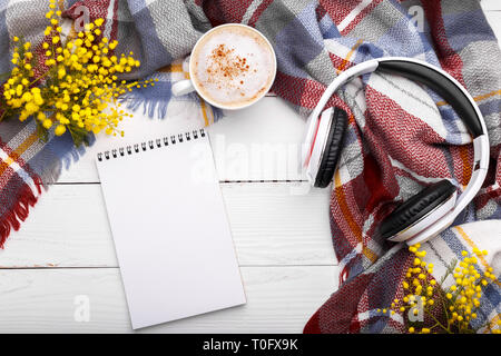 Un café chaud, cappucino, couverture,mimosa,casque et le bloc-notes sur l'ancien fond de bois. Détente romantique saison,concept mise à plat Banque D'Images