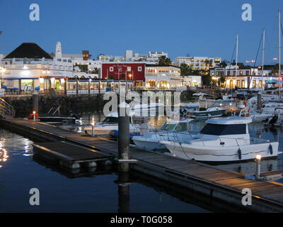 Gamme de yachts et bateaux amarrés jusqu'à une jetée avec les cafés et restaurants éclairés comme l'obscurité ; Marina Rubicon à Playa Blanca. Banque D'Images