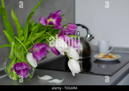 Mauve et blanc tulipes dans un vase transparent sur une table de cuisine. Bon début de journée. Banque D'Images