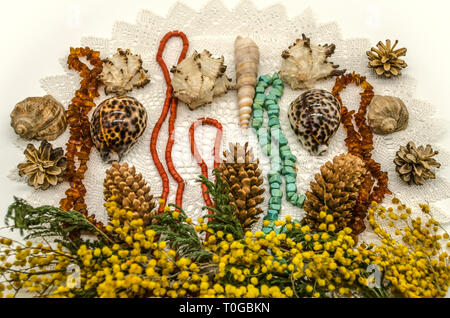 Une frontière de brins de Mimosa jaune avec des pommes de pin, des coquillages et des perles d'ambre, la turquoise et le corail rouge sur les étoffes de laine blanche serviette lacé Banque D'Images