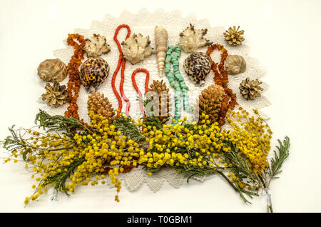 Serviette ajouré blanc tricoté recouvert de pommes de pin, les coquillages et les perles d'ambre, la turquoise et le corail rouge avec des branches de Mimosa jaune Banque D'Images