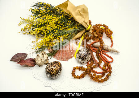 La vie toujours avec un bouquet de mimosas jaunes, enveloppé dans du papier rugueux et attachés à un ruban, avec les coquillages, perles d'ambre et perles de corail sur une délicate w Banque D'Images