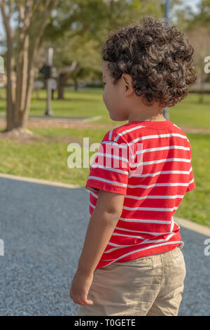 Le petit garçon regarde ailleurs dans le parc. Il recherche les autres enfants jouer avec au parc local. Banque D'Images