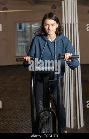 La jeune fille est engagée sur une bicyclette d'exercice crossfit dans la salle de sport Banque D'Images