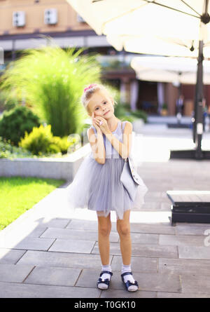 Petit portrait jolie fille se tenant debout dans une cour et le port de robe grise. Banque D'Images