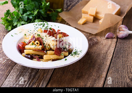 Pâtes rigatoni au salami, poivrons tomates cerises, olives, une délicieuse cuisine italienne servie avec du fromage parmesan râpé sur la table en bois rustique Banque D'Images