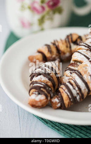 Un plateau de pains au chocolat saupoudré de sucre en poudre, sur une table en bois blanc avec un napperon vert et un verre d'eau dans l'arrière-plan. Banque D'Images