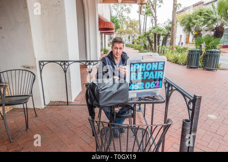 Un réparateur d'iPhone shop met en place sur le trottoir patio d'un café avec un écriteau indiquant 'iPhone' Réparation et son numéro de téléphone. Il tr Banque D'Images