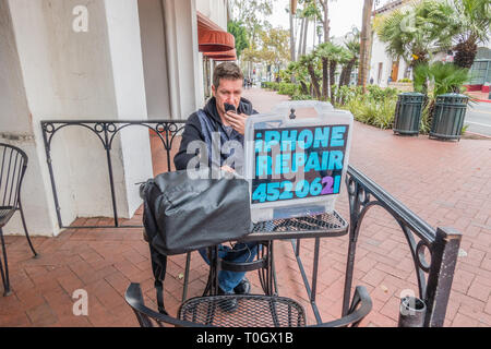 Un réparateur d'iPhone shop met en place sur le trottoir patio d'un café avec un écriteau indiquant 'iPhone' Réparation et son numéro de téléphone. Il tr Banque D'Images