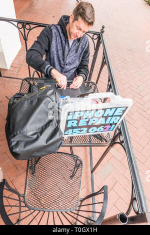 Un réparateur d'iPhone shop met en place sur le trottoir patio d'un café avec un signe 'publicité' de réparation de l'iPhone et son numéro de téléphone. H Banque D'Images