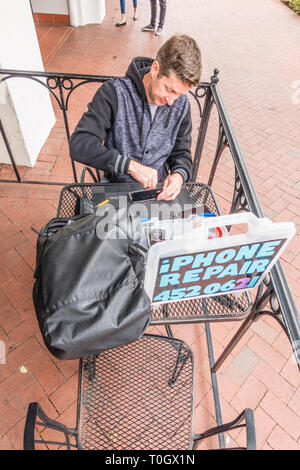 Un réparateur d'iPhone shop met en place sur le trottoir patio d'un café avec un signe 'publicité' de réparation de l'iPhone et son numéro de téléphone. H Banque D'Images