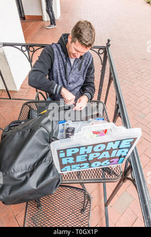 Un réparateur d'iPhone shop met en place sur le trottoir patio d'un café avec un signe 'publicité' de réparation de l'iPhone et son numéro de téléphone. H Banque D'Images