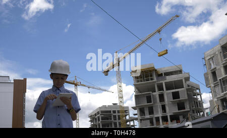 Builder boy stands entre les grues à l'aide de tablet, builder garçon joue un constructeur, s'amuser Banque D'Images