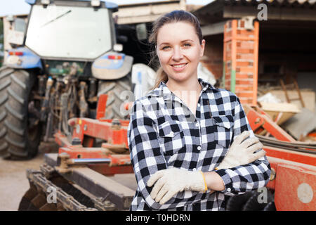 Young woman propriétaire de ferme moderne posant près de tracteur Banque D'Images