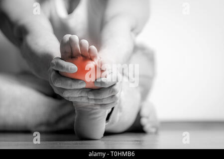 Homme Causian détient les mains pour ses pieds douloureux, des douleurs à pied. La photographie en noir et blanc. Couleur rouge est domaine de la douleur Banque D'Images