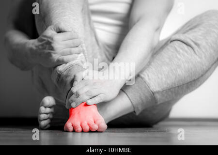 Homme Causian détient les mains pour ses pieds douloureux, des douleurs à pied. La photographie en noir et blanc. Couleur rouge est domaine de la douleur Banque D'Images