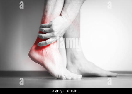 Homme Causian détient les mains pour ses pieds douloureux, des douleurs à pied. La photographie en noir et blanc. Couleur rouge est domaine de la douleur Banque D'Images