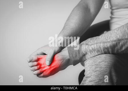 Homme Causian détient les mains pour ses pieds douloureux, des douleurs à pied. La photographie en noir et blanc. Couleur rouge est domaine de la douleur Banque D'Images