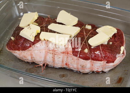 Rôti de bœuf cru avec des morceaux de la margarine sur un plat en verre avant la cuisson Banque D'Images