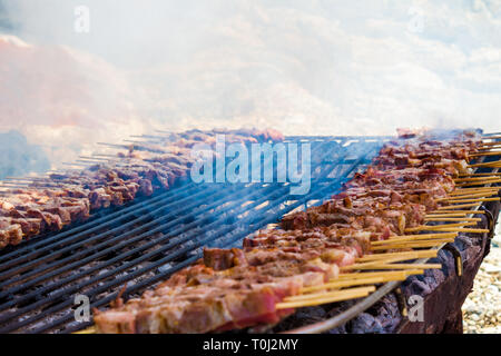 Les brochettes d'agneau et de poulet sur une grille simple et rustique disposés sur le sable d'une île grecque. Close up de Fumeurs Prix de la viande étant cuites. Banque D'Images