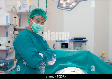 Asian smiling surgeon médecin croisant les bras tout en se tenant dans une salle de chirurgie à l'hôpital. Banque D'Images
