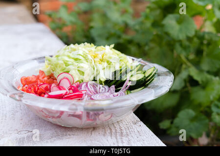 Salade d'été fraîchement coupé. Beaucoup de délicieux légumes dans saladier en verre - concombre, laitue, radis, tomates, oignon rouge Banque D'Images