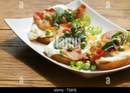 Bruschetta avec rucola, chrispy bacon et œuf poché servi sur plaque blanche. Banque D'Images