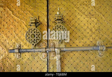 Détail d'un brillant or laiton islamique avec une serrure de porte et deux poignées de portes décorées de façon complexe ; vu à Fès, au Maroc. Banque D'Images