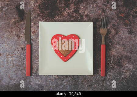 Cœur rouge sur une assiette blanche à côté des couverts contre Grunge background Banque D'Images