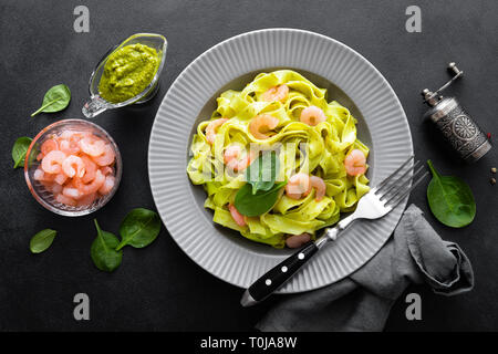 Fettuccine cuits pâtes aux crevettes et pesto d'épinards frais sur fond noir. La cuisine italienne. Plat sain pour le déjeuner. Vue d'en haut Banque D'Images