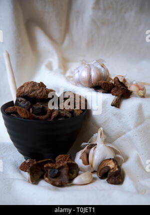 Les champignons séchés avec de l'ail dans une tasse noire sur une nappe de lin blanc Banque D'Images