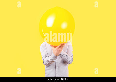 Man holding ballon jaune avec sourire face à l'émotion au lieu de la tête. La pensée positive, les concepts de droit sur un fond jaune Banque D'Images