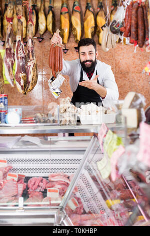 Vendeur mâle montrant les saucisses en boucherie Banque D'Images