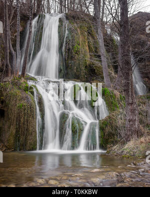 Longue Vue d'exposition d'une cascade ensoleillée avec des jets d'eau tombant roches rouges couvertes par mousse verte Banque D'Images