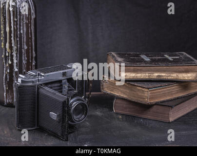 Vieux livres rares en noir couverture cartonnée avec un appareil photo sur un comptoir noir. Banque D'Images