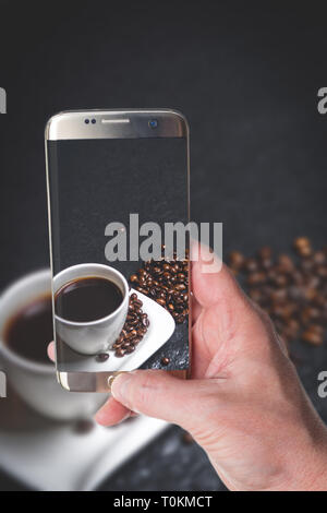 Man taking photo de tasse de café blanc et les grains de café sur la table en pierre noire Banque D'Images