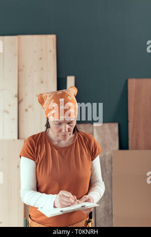 L'auto-portrait utilisé female carpenter writing project notes sur le bloc-notes de presse-papiers dans la petite entreprise de papier l'atelier de menuiserie Banque D'Images