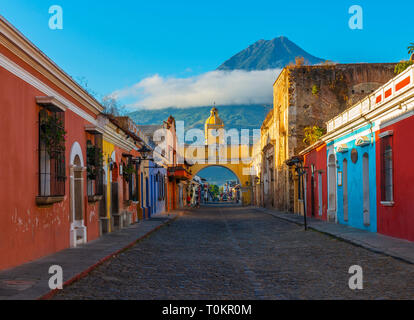 Paysage urbain de la rue principale et jaune Santa Catalina arch dans le centre-ville historique d'Antigua au lever du soleil avec le volcan Agua, au Guatemala. Banque D'Images