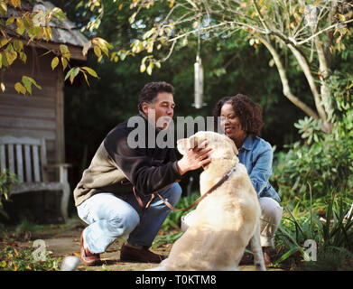 Happy mid-adult couple tapotant leur chien dans la cour arrière de leur maison. Banque D'Images