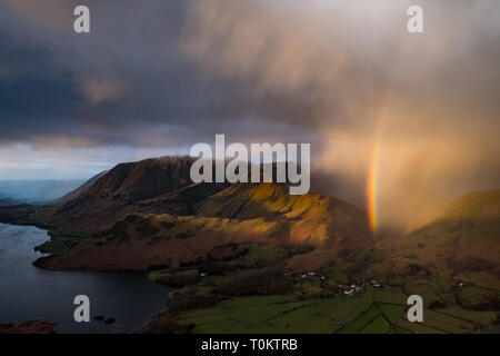 Une douche passe au-dessus de Crummock Water, Grasmoor Rannerdale Whiteless, noeuds, Pike et Buttermere village, produisant un arc-en-ciel vif. Lake District, UK Banque D'Images