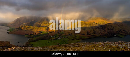 Une douche passe au-dessus de Crummock Water, Grasmoor Rannerdale Whiteless, noeuds, Pike et Buttermere village, produisant un arc-en-ciel vif. Lake District, UK Banque D'Images