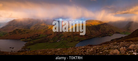 Une douche passe au-dessus de Crummock Water, Grasmoor Rannerdale Whiteless, noeuds, Pike et Buttermere village, produisant un arc-en-ciel vif. Lake District, UK Banque D'Images