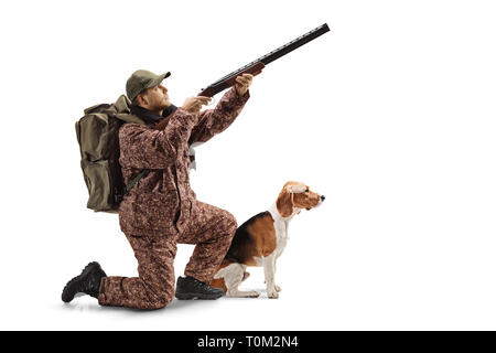 D'un coup pleine longueur genoux avec un fusil de chasse, visant vers le haut et un chien beagle à côté de lui isolé sur fond blanc Banque D'Images