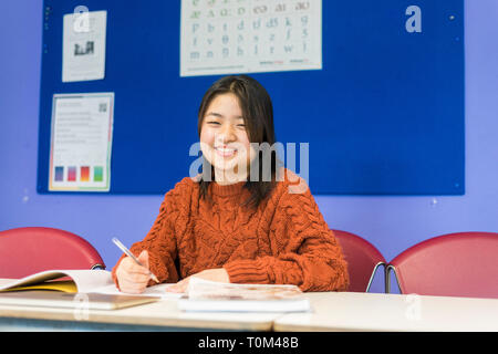 Un jeune étudiant asiatique est assis à un bureau dans une salle de classe à étudier au cours de sa leçon. Banque D'Images